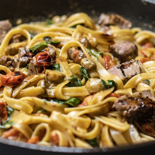 Fresh pasta with mushrooms, tomatoes, greens and sliced steak